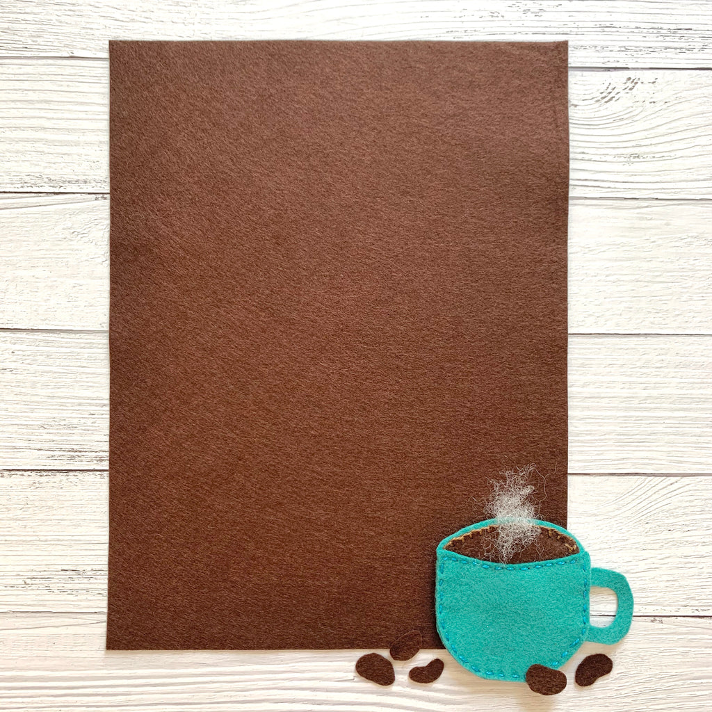 one 8 x 10 sheet of brown colored felt on a white wood background with a teal coffee cup made of felt 