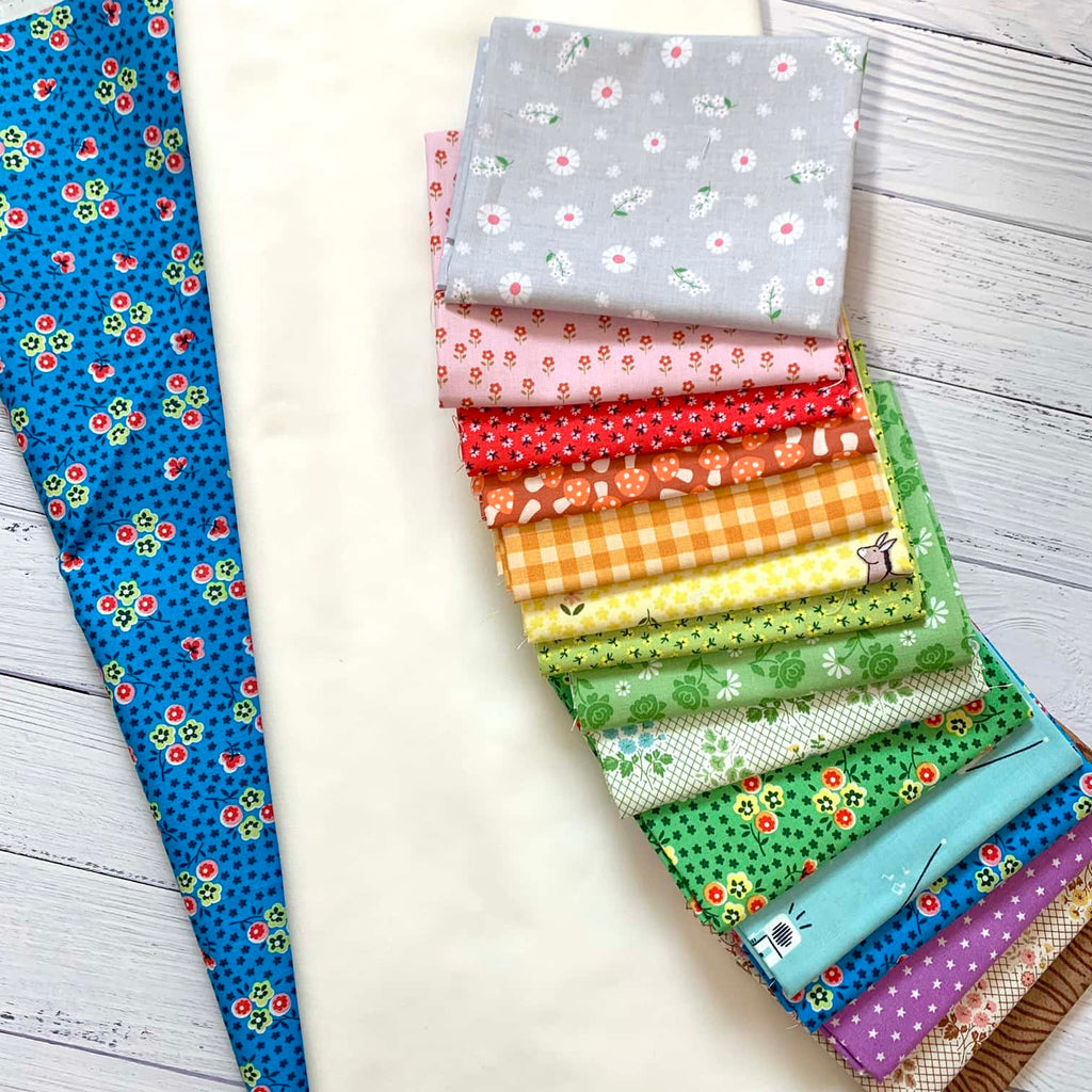 a row of fabric fat quarters arranged in rainbow order on top of white fabric.