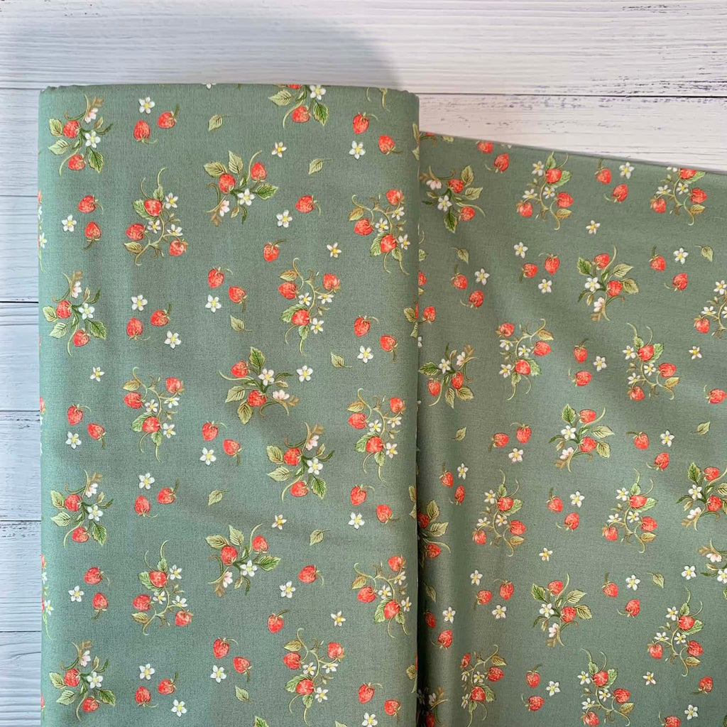 a bolt of quilting cotton fabric that features cottage core style strawberries repeated over a sage green background