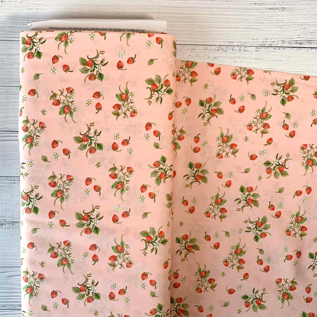 a bolt of quilting fabric featuring illustrated strawberries repeated over a pink background