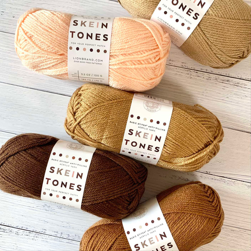 5 skeins of various skin tone colored yarn arranged on a white wood background.