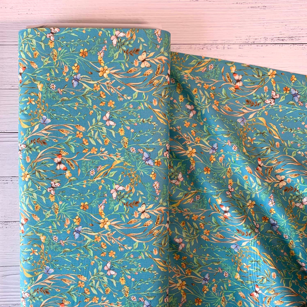 a bolt of quilting fabric that features wildflowers and butterflies repeating over a teal background.