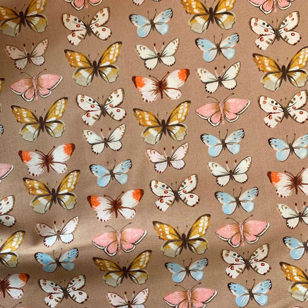 a closeup of quilting fabric that features butterflies repeated over a mauve background