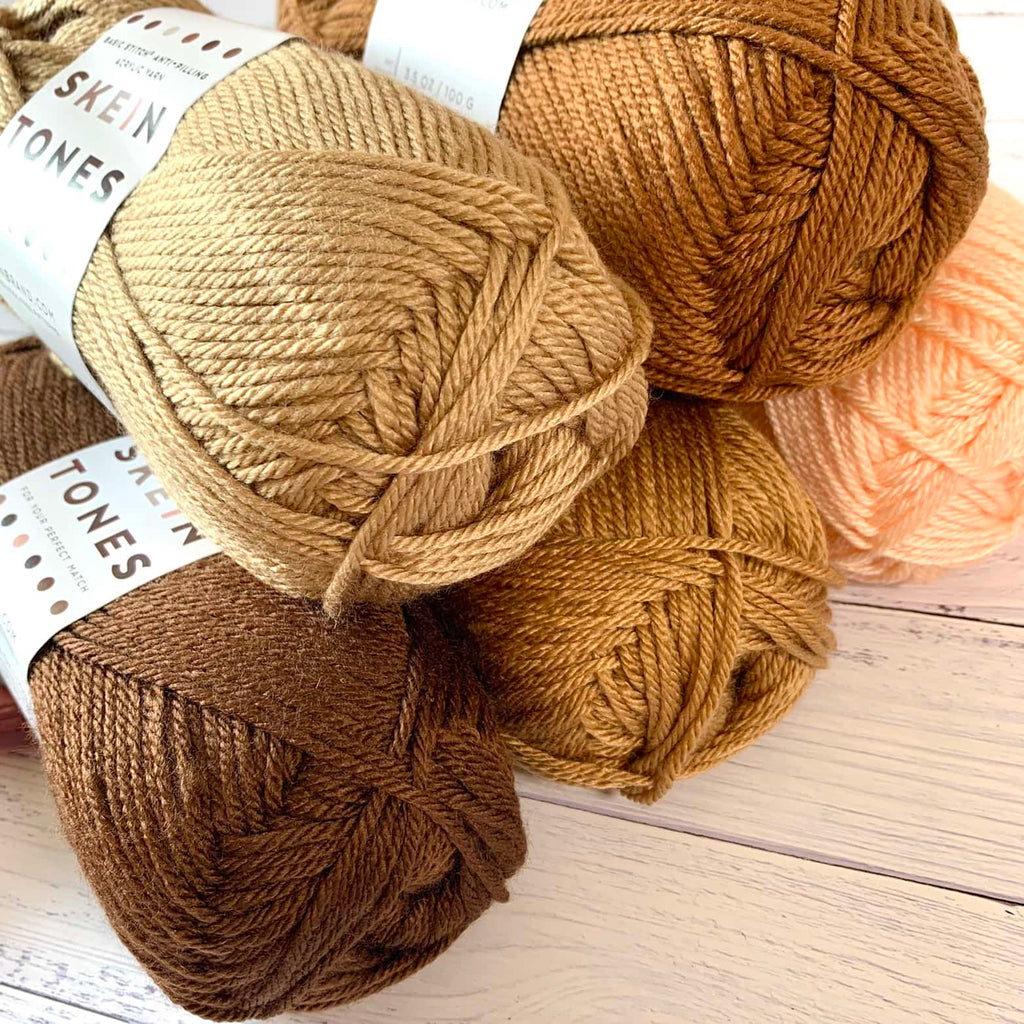 5 skeins of various skin tone colored yarn arranged in a a stack