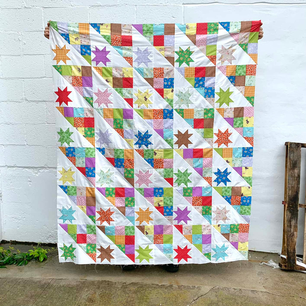 Colorful Patchwork quilt being held up against a white wall