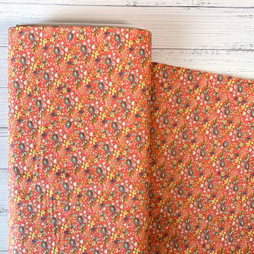 a bolt of quilting cotton fabric featuring ditsy florals repeated over a red background